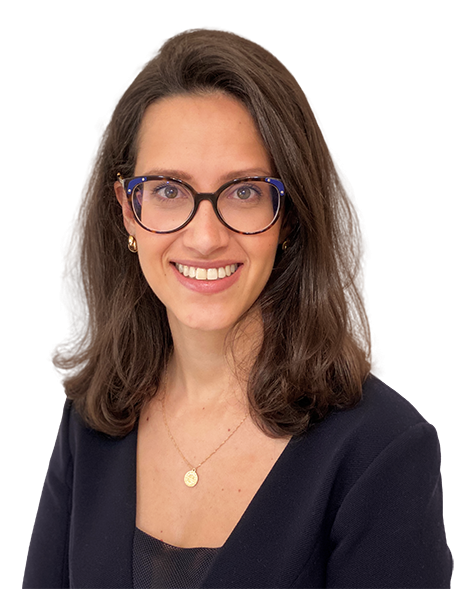 Camilla possui cabelos castanhos levemente ondulados. Usa óculos de grau com formato arredondado, e está usando blusa preta de manga longa com poás. Está com um largo sorriso.