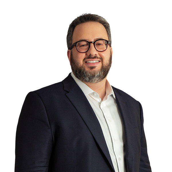 O sócio Guilherme Bouzan tem cabelos e barba grizalhos. Ele veste um paletó preto com camisa social branca. Na foto, está usando óculos e com um sorriso.