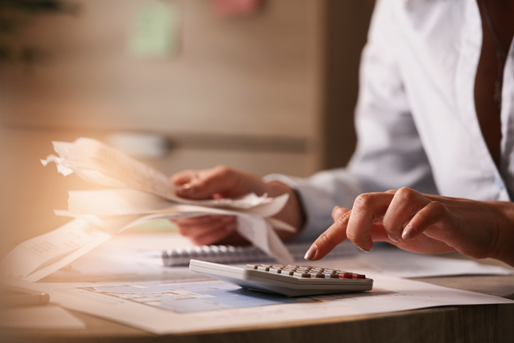 mãos de uma mulher segurando papéis em uma e utilizando calculador com a outra