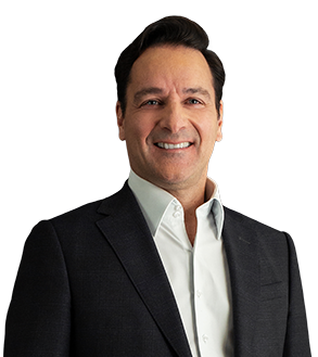 Sócio João Colussi está vestindo um blazer preto e uma camisa social branca. Ele tem o cabelo curto e preto, repartido para o lado. Ele está com um largo sorriso