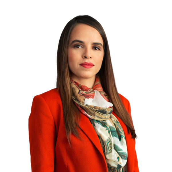 A sócia ariane possui cabelos longos, castanhos, com as pontas mais claras. Na foto, está com uma expressão leve e alegre. Está usando blazer vermelho, com lenço estampado, e batom rosa.