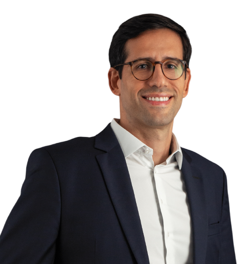 Bruno veste um paletó preto com camisa social branca. Na foto, está usando óculos com um largo sorriso. Seus cabelos são castanho escuro.