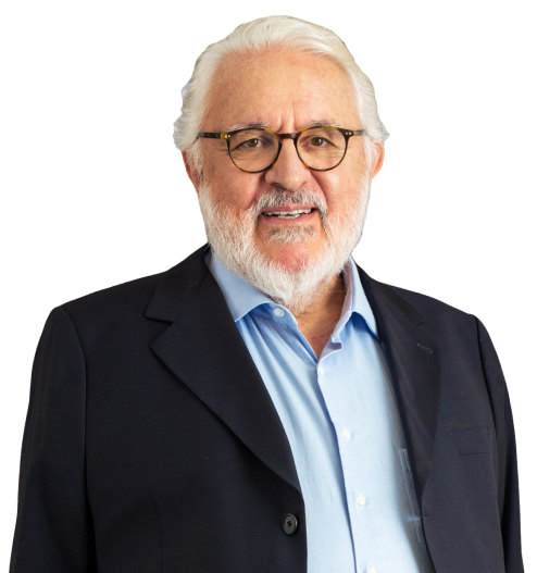 Sócio-Fundador Otávio Veiga está vestindo um terno escuro e camisa azul claro. Ele tem barba, bigode e cabelo brancos e usa óculos. Ela está com um largo sorriso.