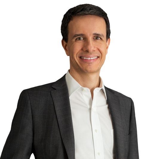 Sócio Paulo Brancher está vestindo um terno preto e camisa branca. Ele tem cabelo castanho escuro e está com um largo sorriso.