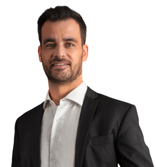 Sócio Paulo Tedesco está vestindo um terno preto e camisa branca. Ele tem cabelo, barba e bigode castanho escuro e está com um leve sorriso.