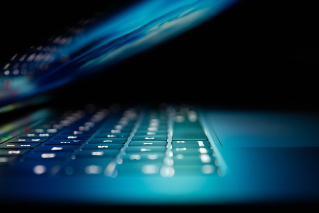 Um laptop aberto, com a tela ligada, refletindo uma luz azul sobre o teclado