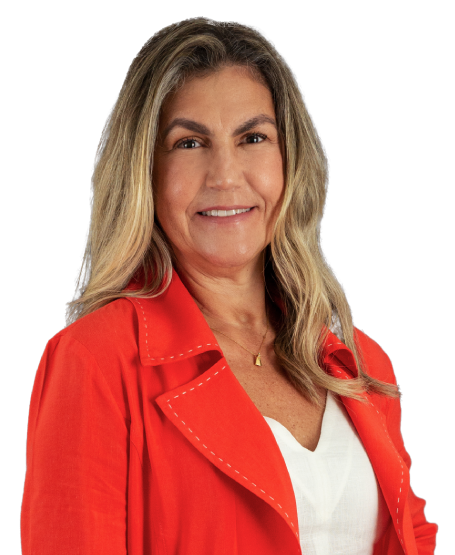 Sócia Rossana Duarte está vestindo um conjunto de blusa e bermuda laranja com camisa branca. Tem cabelo loiro, pouco abaixo dos ombros, usa um colar dourado e está com um largo sorriso.