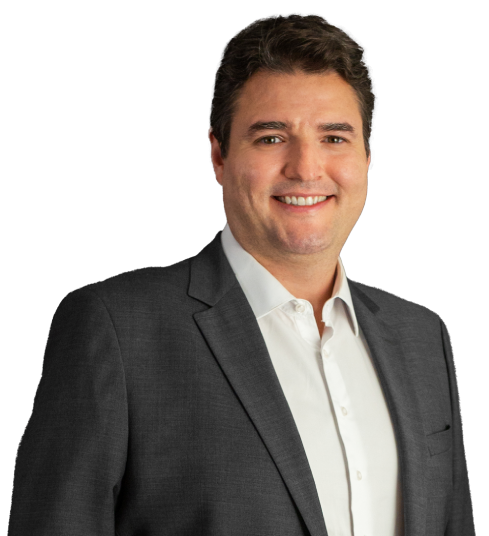 O sócio Thiago Jabor está vestindo um paletó cinza escuro e camisa social branca. Ele tem cabelos castanho escuro. Está com um largo sorriso na foto.