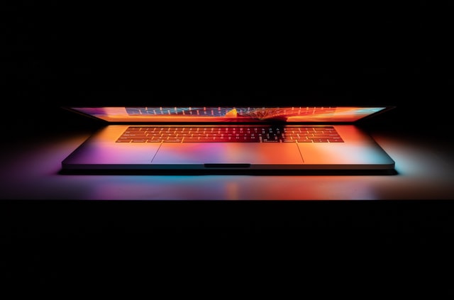 Um notebook aberto refletindo a tela colorida no teclado, o fundo da imagem é preto