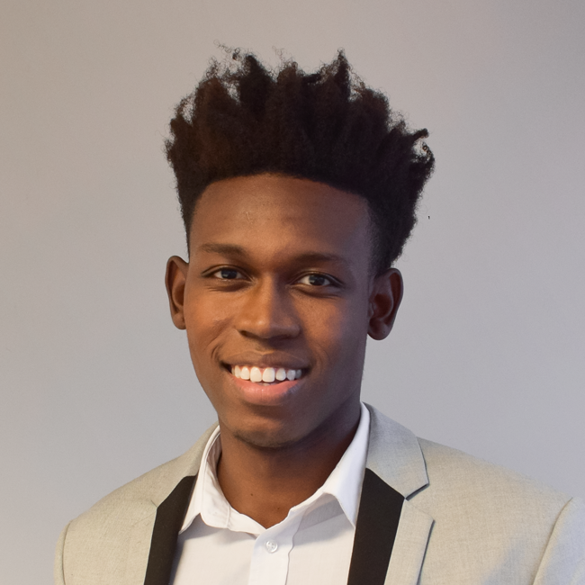 Eder é negro e usa cabelo black. Na foto está usando camisa social branca e está com um largo sorriso.