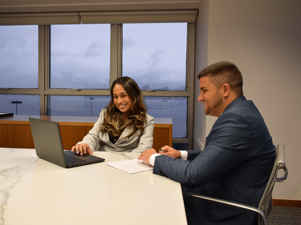 dois jovens, um rapaz e uma moça, sentados em uma sala de reunião, trabalhando juntos no notebook