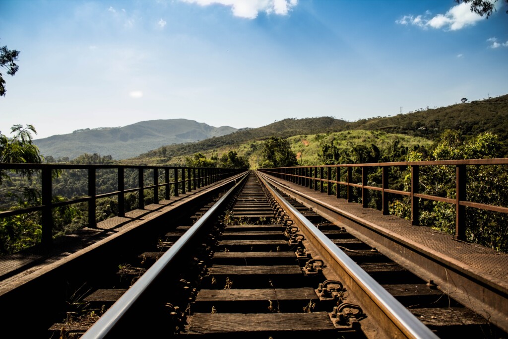 uma ferrovia com a vista de um campo verde ao fundo e o céu azul
