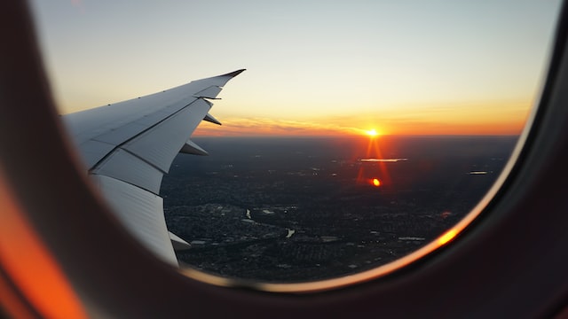 Uma janela de avião com a visão das asas e o por do sol