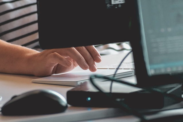 Mesa com mouse e computador, um modem e as mãos de uma mulher branca escrevendo no teclado