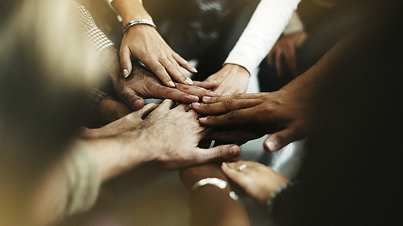 Foto de diversas pessoas, de diferentes etnias, juntando as mãos