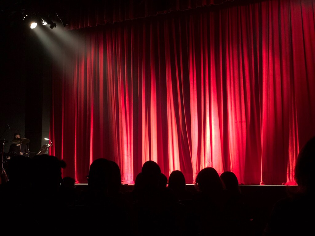 pessoas esperando a cortina ser aberta em um teatro.