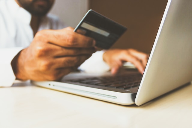 Homem de camisa branca fazendo compras online com seu notebook branco e um cartão black