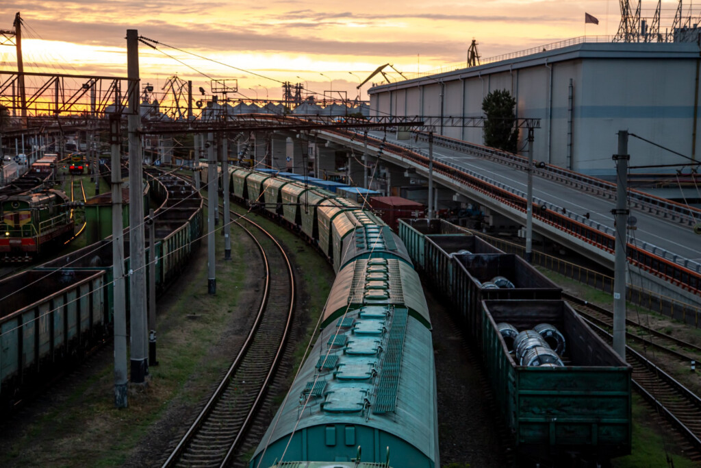 Ferroviária de cargas. Trilho, trem e cargas ao lado.