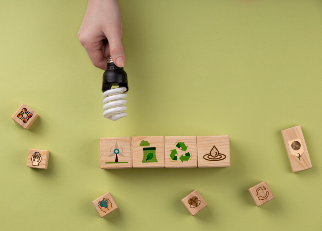 Sustentabilidade. Mão segurando lâmpada e quadrinhos com desenhos sustentáveis sobre uma mesa verde.