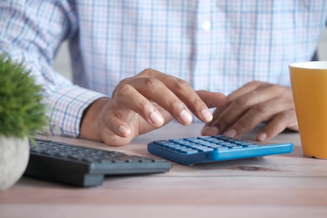Homem fazendo conta em calculadora com um teclado de computador ao lado
