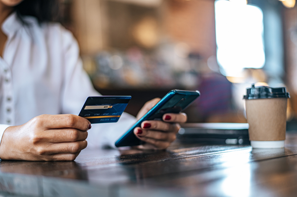 Mulher comprando  mercadorias com cartão de crédito através de um smartphone em uma cafeteria.