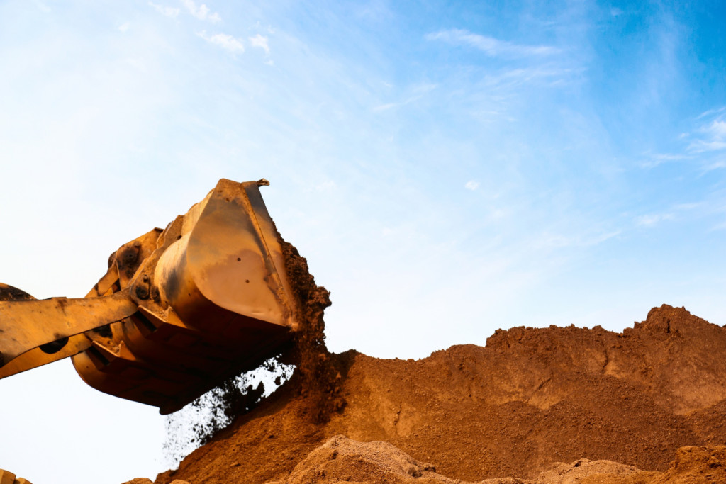 A imagem mostra pá de uma escavadora removendo areia de um monte
