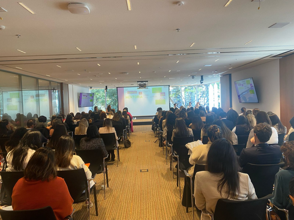 Sala com cadeiras e um palco, como se fosse um mini auditório, mostrando a plateia do evento