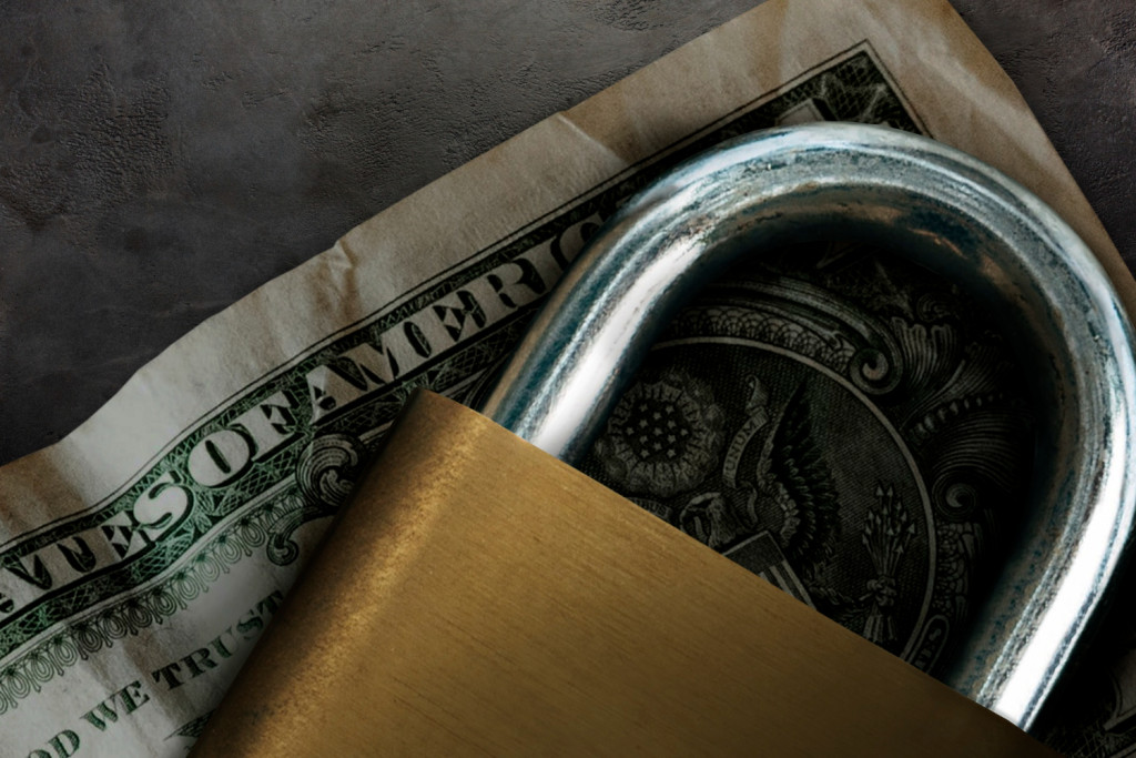 Nota de dólar envelhecida embaixo de um cadeado fechado.