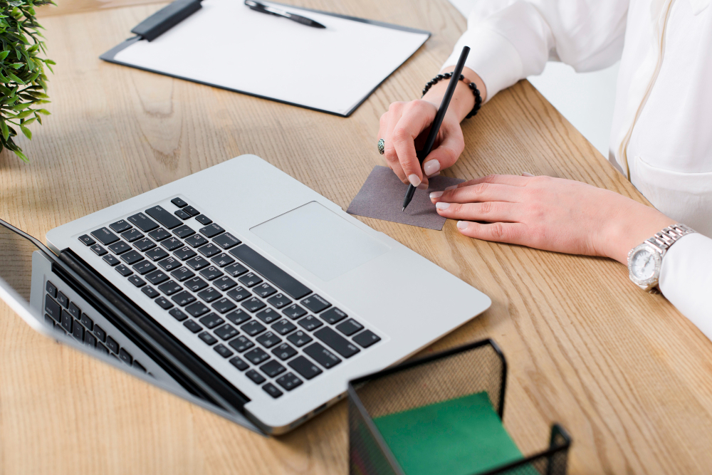Pessoa escrevendo na nota com caneta sobre a mesa de madeira com laptop