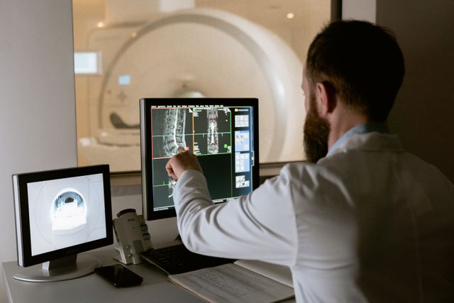 Profissional médico revisando exames de ressonância magnética em telas de computador para fins diagnósticos.